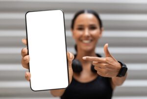 Fitness App. Sporty Young Woman Pointing At Big Blank Smartphone In Hand