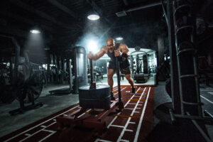 Bodybuilder athlete working out in the gym. Strong and fit man training with crossfit sled. Sport and fitness motivation. Individual sports recreation.